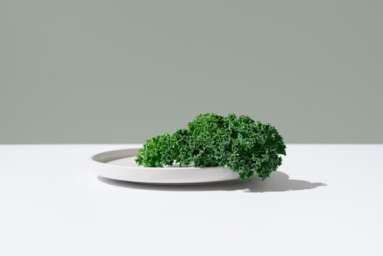 Hojas de col rizada verde fresca en un plato blanco sobre fondo verde