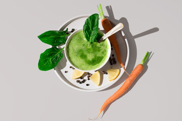 Sopa de espinacas con hojas de espinacas y zanahorias en un recipiente blanco sobre fondo beige. Vista superior