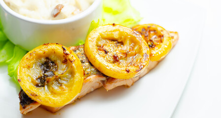A plate of food with a piece of salmon and a couple of yellow slices of lemon