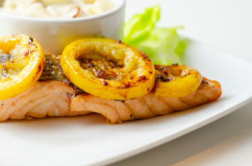 A plate of food with a piece of salmon and a couple of yellow slices of lemon