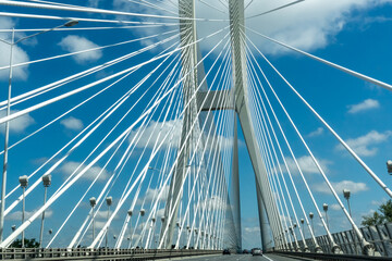 Naklejka premium Suspension bridge with cars driving under a bright blue sky with white clouds. High quality photo