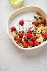 Serving bowl with greek yogurt, fresh strawberries, breakfast flakes and granola, vertical shot on a light-beige stone background, high angle view