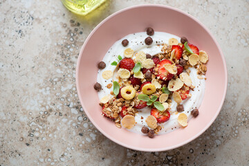 Breakfast yogurt bowl with strawberry, granola and flakes, horizontal shot on a beige granite background, high angle view