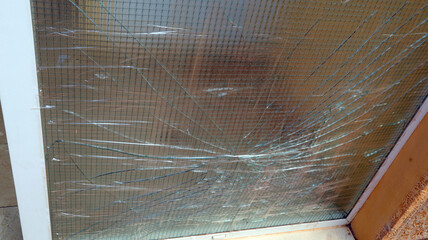 Close-up view of broken windowpane with a wire mesh behind it. Glass is shattered with numerous...