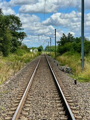 Long, Straight Railway Track Extending into the Distance Amidst Lush Greenery and Blue Sky with Fluffy Clouds