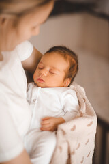 Mother holding infant baby boy 1-2 months old sleeping on hands in room. Motherhood.