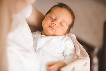 Mother holding infant baby boy 1-2 months old sleeping on hands in room. Motherhood.