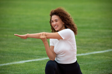 Curly beautiful Asian girl in a white T-shirt and black leggings plays sports on the football field