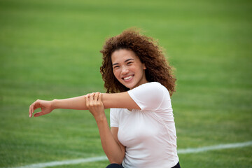 Curly beautiful Asian girl in a white T-shirt and black leggings plays sports on the football field