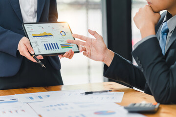 Two professionals analyzing business data on dashboard screen and discussing financial graphs and charts in a modern office.