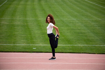 Curly beautiful Asian girl in a white T-shirt and black leggings plays sports on the football field