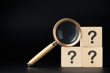 Magnifying glass and stack of question mark wood cubes, analyze the questions, FAQs, and questions...