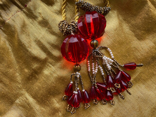 A big red bead with intricate golden and white beads latkans on golden fabric is a striking and...