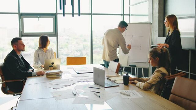 In a contemporary workspace, a diverse team of young professionals collaborate in a lively business meeting, exchanging ideas and strategies for innovation and efficiency