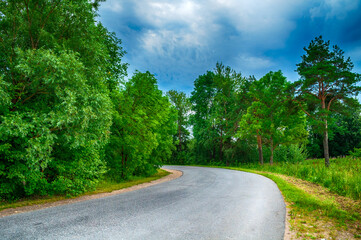 Summer landscape, suburban road receding into the distance under dramatic cloudy sky.