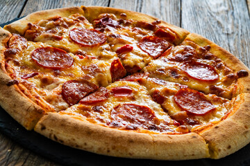 Circle pizza chorizo and mozzarella served on stony black plate on wooden table
