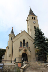 Church building with tall clock tower standing on a hill with stone steps leading to the front door, Tokaj, Hungary