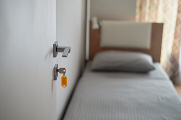 Room reservation. The key is in the door, and the bed is out of focus. Travel in simple conditions. Rental housing.