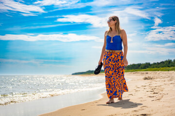 Summer holidays on beach by Baltic Sea . Beautiful young woman in blue swimsuit and patterned skirt...