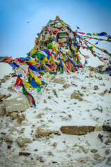 A pile of colorful prayer flags, some faded and tattered, resting in the snow.