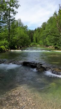 Aerial Drohnenflug in niedriger H&ouml;he &uuml;ber eine Stromschnelle in einem Fluss mit kristallklarem Wasser in den Alpen mit Wald, B&auml;umen und blauem Himmel, Hochformat, UHD