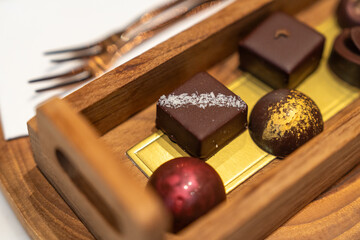 Various flavored chocolate candies in a wooden tray on a table in a cafe. Top view.
