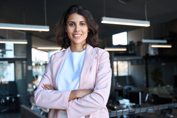 Portrait of successful hispanic young business woman with crossed arms smiling confident at camera....