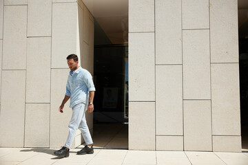 Young man walking past a modern building, dressed casually in light denim, looking thoughtful and focused.