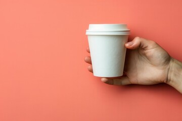 Hand holding a white disposable coffee cup against a coral background. Perfect for coffee shop promotions and branding materials.