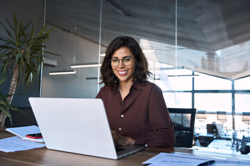 Smiling 30s latin hispanic middle-aged business woman working on laptop computer in modern office....
