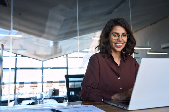 Happy latin hispanic young business woman working on laptop computer in company office. Smiling Indian entrepreneur manager businesswoman using pc for communication, learning at workplace. Copy space