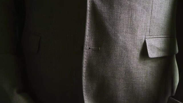 a man fastens a button on his jacket. the guy is wearing a tuxedo. the groom is preparing for a wedding event