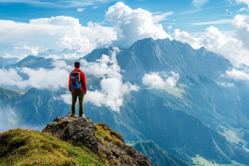 A man stands atop a mountain peak, taking in the breathtaking panoramic view of the surrounding mountains and valleys, enveloped by clouds and the vast blue sky.