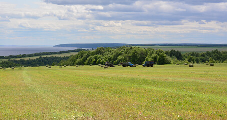 Fototapeta premium a field with tractors, haybales and a blue sky with a few clouds 