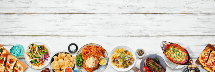 Bottom border of various delicious foods. Top down view on a white wood banner background. Copy space. Pastas, flatbreads, tacos, steak and restaurant theme dishes.