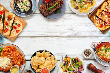 Frame of various delicious foods. Overhead view on a white wood background. Copy space. Pastas, flatbreads, tacos, steak and restaurant theme dishes.