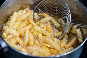 Potatoes in boiling oil, homemade french fries, deep fried potato cooking in metal fryer pot, fat...