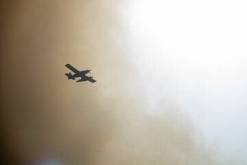 Firefighting plane flying into a large smoke cloud caused by a forest fire