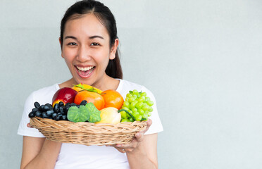 Young smiling woman posing with basket of fresh vegetables. Time of healthy food, bananas, apple, tomato, green grapes. Vegetables and Fruits.