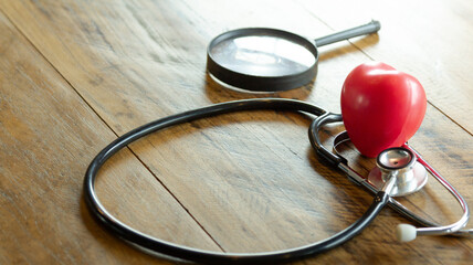 Black stethoscope with red heart of doctor for check up on wooden table background. Stethoscope equipment of medical use to diagnose hear sound. Health care.