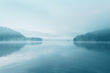 Obraz premium A serene lake surrounded by mist-shrouded forest and distant hills, creating an ethereal landscape that exudes tranquility and a sense of untouched natural beauty.