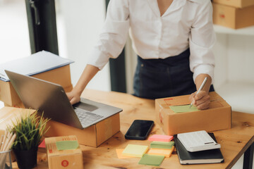 beautiful asian woman working at home selling online with yellow box and laptop on taking name orders from customers sme business concept parcel delivery