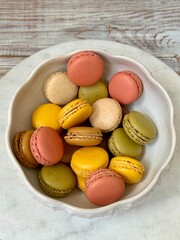 Macarons in different colors and tastes in the white plate on the marble and wooden background 