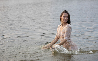 Sexy attractive girl in a white see-through dress is bathing in the water in the evening