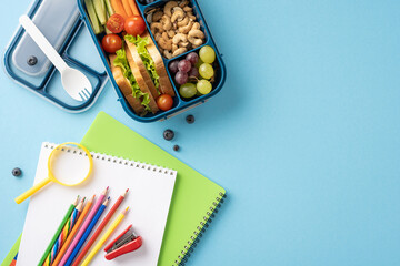 Top view of a healthy school lunchbox, notebook, and colorful pencils arranged on a blue background