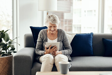 Obraz premium Senior woman, tablet and home with online, game app or social media scroll for news in retirement. Lounge, sofa and smile with web, tech and relax in living room with soap opera streaming at morning