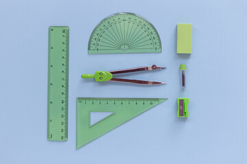 Green Set of geometry tools with compass, rulers, sharpener and eraser lies on a blue background, top view