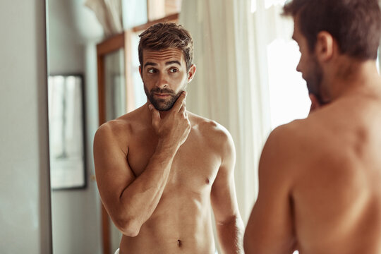 Man, bathroom and cosmetics with reflection in morning for grooming routine, skincare and self care for beard. Person, topless and cleaning face for glowing skin, hygiene and getting ready in mirror
