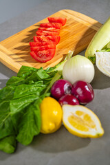 Various vegetables are lying on the table, wooden cutting board with sliced tomatoes displayed on top