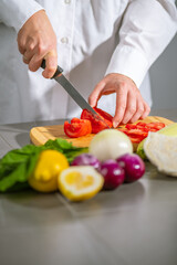 A chef is cutting various vegetables on a wooden cutting board in the kitchen